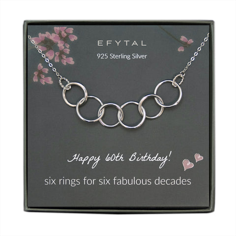 grey jewelry box containing silver necklace with six thick interlocking rings, placed on a grey card with pink flowers at the top. the text on the card reads "EFYTAL 925 sterling silver" at the top and "Happy 60th Birthday! six rings for six fabulous decades" at the bottom.