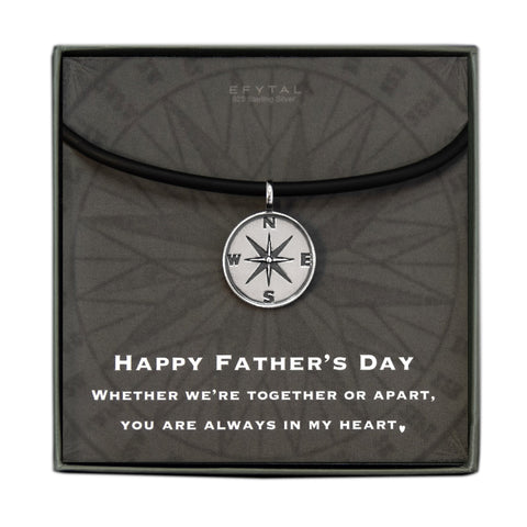 A grey jewelry box containing a grey message card with tonal compass motif. A black silicone cord with a Sterling Silver compass pendant rests on the card. The white text on the card reads “EFYTAL 925 Sterling Silver” at the top and “HAPPY FATHER’S DAY WHETHER WE’RE TOGETHER OR APART, YOU ARE ALWAYS IN MY HEART <3 .”  