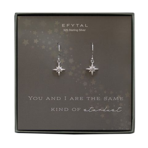 A grey jewelry box containing a grey message card with a diagonal star motif from top left corner to bottom right corner. A pair of star shaped dangle earrings with CZ stones rests on the card. The white text on the card reads “EFYTAL 925 Sterling Silver” at the top and “YOU AND I ARE THE SAME KIND OF STARDUST” at the bottom.  