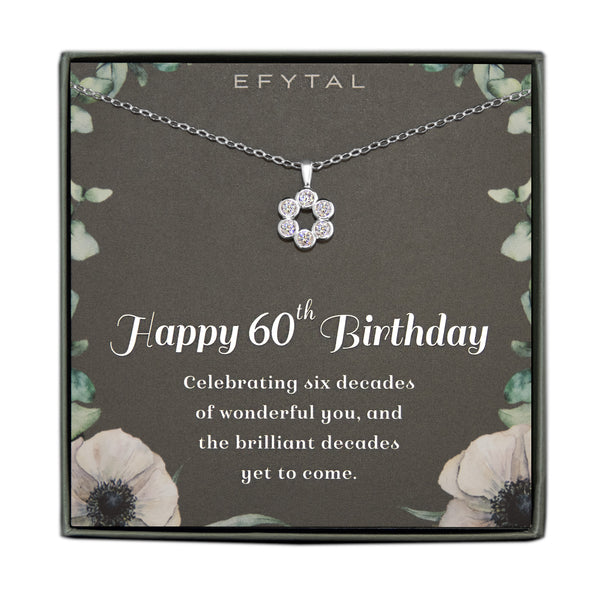 Grey jewelry box containing a silver necklace with a cluster of 6 cz stones, placed on a grey card with a border of green leaves and two anemone flowers in the bottom corners. The text on the card reads "EFYTAL" at the top and "Happy 60th Birthday. Celebrating six decades of wonderful you and the brilliant decades yet to come" on the bottom.