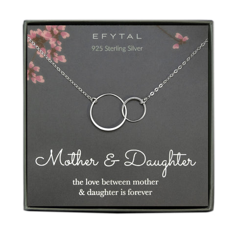 A grey jewelry box holds a grey message card with pink flower motif at the top. A sterling silver necklace with two joined rings rests on the card. The text above the necklace reads "EFYTAL 925 Sterling Silver" in cream text. Underneath the necklace, the text reads "Mother & Daughter the love between mother & daughter is forever"
