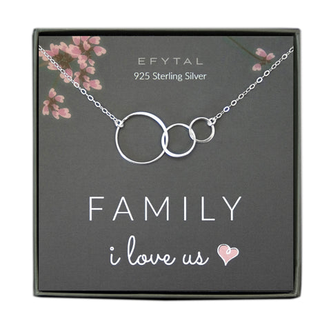 A grey jewelry box containing a grey message card with pink floral motif in the upper corners. A 925 Sterling Silver necklace with three interlocking rings of various size rests on the card. The white text on the card reads “EFYTAL 925 Sterling Silver” at the top and “FAMILY I love us <3” at the bottom.