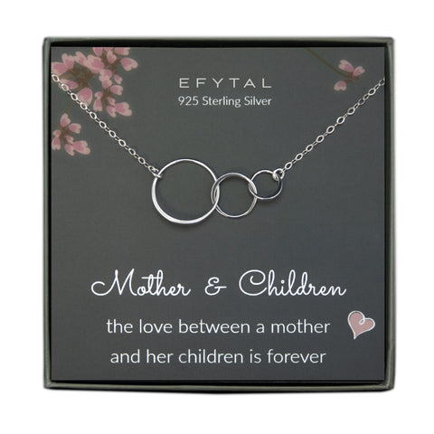grey jewelry box containing silver necklace with three thin interlocking circles, placed on a grey card with pink flowers and branches at the top. the text on the card reads "EFYTAL 925 sterling silver" at the top and "Mother & Children - the love between mother <3 & her children is forever" at the bottom.