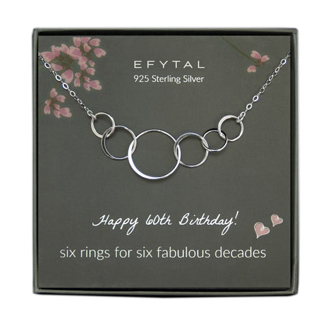 grey jewelry box containing silver necklace with six thin interlocking circles, placed on a grey card with pink flowers and branches at the top. the text on the card reads "EFYTAL 925 sterling silver" at the top and "Happy 60th Birthday! six rings for six fabulous decades <3 <3" at the bottom.