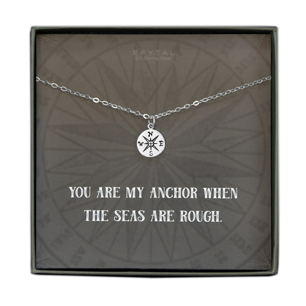 A grey jewelry box containing a grey message card with tonal compass motif. A 925 Sterling Silver ball chain with a small Sterling Silver compass pendant rests on the card. The white text on the card reads “EFYTAL 925 Sterling Silver” at the top and “YOU ARE MY ANCHOR WHEN THE SEAS ARE ROUGH.”  