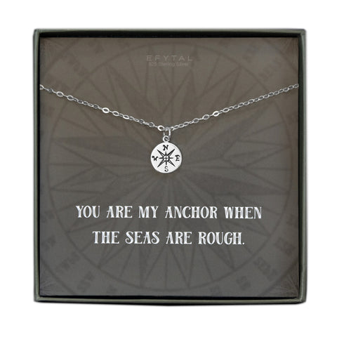 A grey jewelry box containing a grey message card with tonal compass motif. A 925 Sterling Silver ball chain with a small Sterling Silver compass pendant rests on the card. The white text on the card reads “EFYTAL 925 Sterling Silver” at the top and “YOU ARE MY ANCHOR WHEN THE SEAS ARE ROUGH.”  