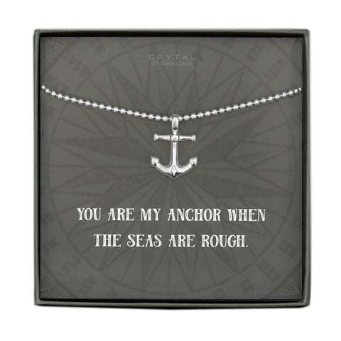 A grey jewelry box containing a grey message card with tonal compass motif. A 925 Sterling Silver ball chain with a Sterling Silver anchor pendant rests on the card. The white text on the card reads “EFYTAL 925 Sterling Silver” at the top and “YOU ARE MY ANCHOR WHEN THE SEAS ARE ROUGH.”  