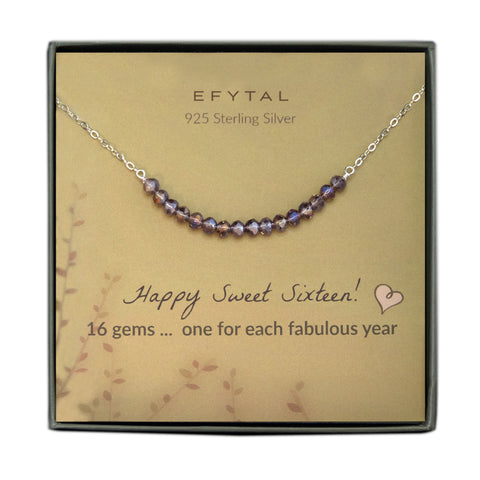 grey jewelry box containing silver necklace with sixteen iridescent purple glass beads, placed on a faded yellow card with a branch motif in the lower left corner. the text on the card reads "EFYTAL 925 sterling silver" in brown at the top and "Happy Sweet Sixteen! 16 gems...one for each fabulous year" at the bottom.