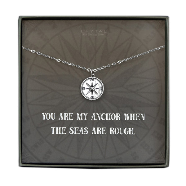 A grey jewelry box containing a grey message card with tonal compass motif. A 925 Sterling Silver ball chain with a Sterling Silver compass pendant rests on the card. The white text on the card reads “EFYTAL 925 Sterling Silver” at the top and “YOU ARE MY ANCHOR WHEN THE SEAS ARE ROUGH.”  