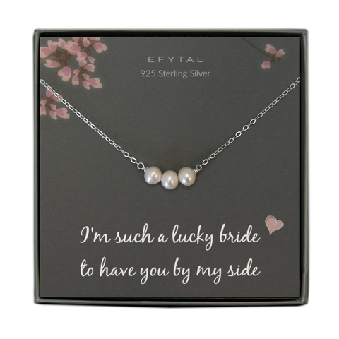 A grey jewelry box containing a grey message card with pink flower motif at the top.  A sterling silver necklace with a row of three cream pearls in the center rests on the card. The white text on the card reads “EFYTAL 925 Sterling Silver” at the top and “I’m such a lucky bride <3 to have you by my side” at the bottom. 