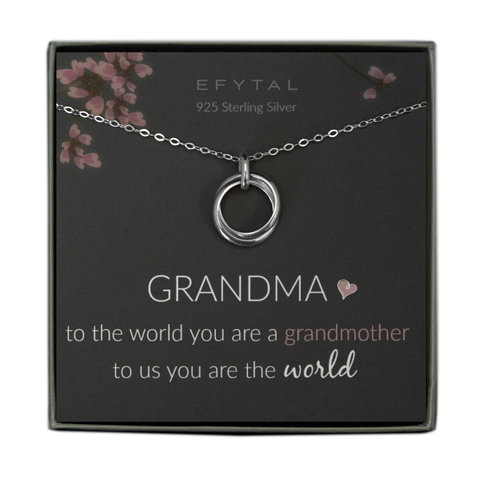 A grey jewelry box contains a grey message card with pink flower and branch motifs at the top. A sterling silver necklace with a pendant of two thick interlocking rings rests on the card. The text at the top of the card reads "EFYTAL 925 Sterling Silver" and, at the bottom: "GRANDMA <3 to the world you are a grandmother to us you are the world"