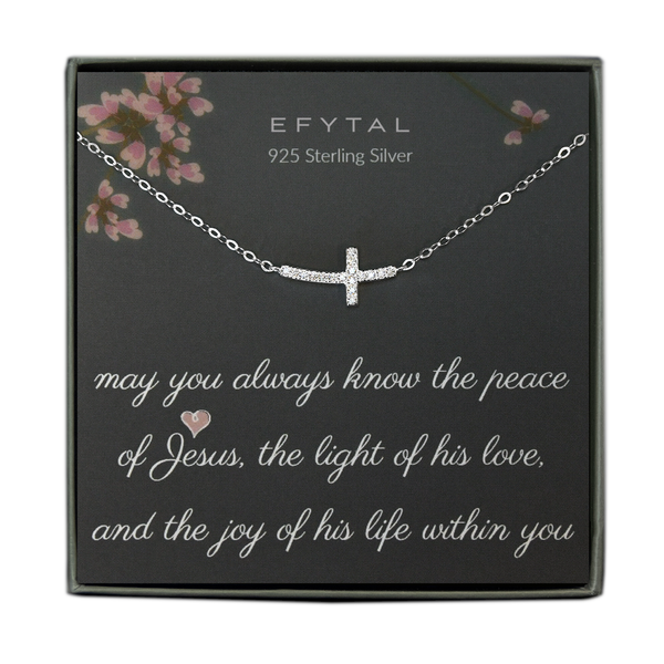 A grey jewelry box contains a grey message card with pink flower and branch motifs at the top. A sterling silver necklace with a sideways cz encrusted cross necklace rests on the card. The white text on the card reads "EFYTAL 925 Sterling Silver" at the top and "may you always know the peace of Jesus, the light of his love, and the joy of his life within you"