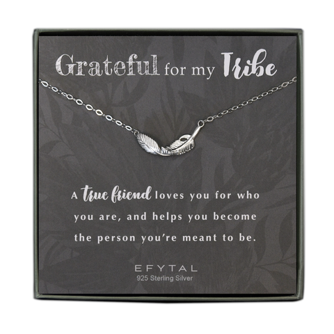 A grey jewelry box contains a grey message card with allover faded floral motif. A necklace with a textured sterling silver feather pendant rests on the card. The text above the necklace reads "Grateful for my Tribe" and the text below reads "A true friend loves you for who you are, and helps you become the person you're meant to be. EFYTAL 925 Sterling Silver"