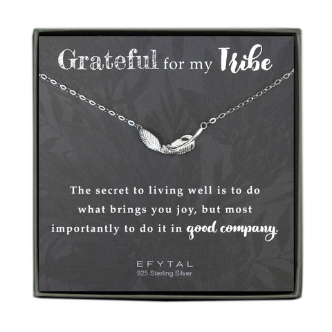  grey jewelry box contains a grey message card with allover faded floral motif. A necklace with a textured sterling silver feather pendant rests on the card. The text above the necklace reads "Grateful for my Tribe" and the text below reads “The secret to living well is to do what brings your joy, but most importantly to do it in good company. EFYTAL 925 Sterling Silver"