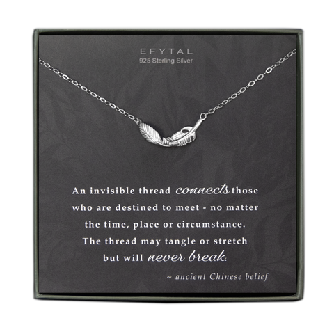 A grey jewelry box contains a grey message card with a faded grey floral motif all over. A sterling silver necklace with a dimensional feather pendant rests on the card. The white text at the top of the card reads "EFYTAL 925 Sterling Silver" and the white text at the bottom reads "An invisible thread connects those who are destined to meet - no matter the time, place, or circumstance. The thread may tangle or stretch but it will never break. - ancient Chinese belief"