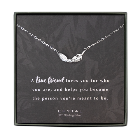 A grey jewelry box contains a grey notecard with allover faded grey floral motif. A necklace with a sterling silver necklace with a textured feather pendant rests across the card. The white text below the necklace reads "A true friend loves you for who you are, and helps you become the person you're meant to be. EFYTAL 925 Sterling Silver" 