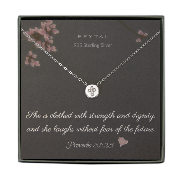 A grey jewelry box containing a grey message card with pink flower motif at the top.  A sterling silver necklace with a small circular pendant rests on the card. There is a cz cross embedded in the center of the pendant. The white text on the card reads “EFYTAL 925 Sterling Silver” at the top and “She is clothed with strength and dignity, and she laughs without fear of the future Proverbs 31:25 <3” at the bottom. 
