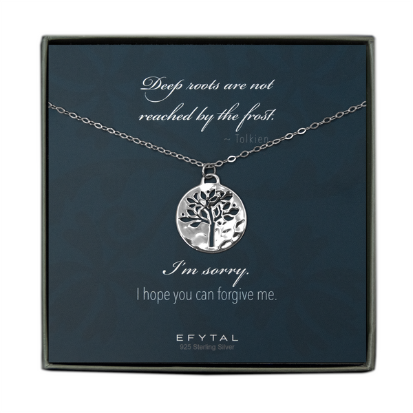 A grey jewelry box golds a blue message card with floral patterned background. A sterling silver necklace rests on the card. The necklace has a hammered pendant with a tree shaped cutout. The white text on the card reads “Deep roots are not reached by the frost. ~ Tolkein” at the top and "I’m sorry. I hope you can forgive me. EFYTAL925 Sterling Silver” on the bottom.