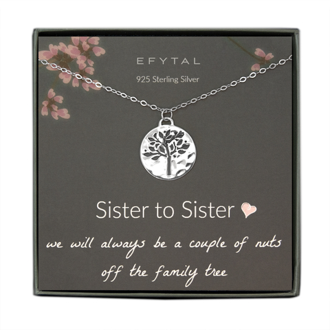 A grey jewelry box containing a grey message card with pink flower motif at the top.  A sterling silver necklace rests on the card. The necklace has a hammered pendant with a tree shaped cutout. The white text on the card reads “EFYTAL 925 Sterling Silver” at the top and “Sister to Sister <3 we will always be a couple of nuts off the family tree”