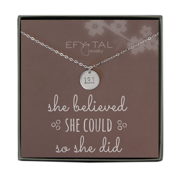 A grey jewelry box holds a mauve message card with white flower motif at the top right corner. A sterling silver necklace with a disc pendant engraved with “13.1” rests on the card. The text above the necklace reads "EFYTAL Jewelry” in white text. Underneath the necklace, the text reads “she believed SHE COULD so she did.”