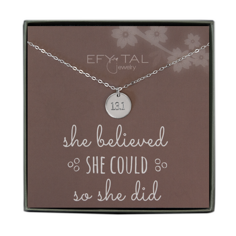 A grey jewelry box holds a mauve message card with white flower motif at the top right corner. A sterling silver necklace with a disc pendant engraved with “13.1” rests on the card. The text above the necklace reads "EFYTAL Jewelry” in white text. Underneath the necklace, the text reads “she believed SHE COULD so she did.”