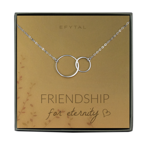 A green jewelry box holds a yellow jewelry card with brown leaf motif in the bottom left corner. A sterling silver necklace with two interlocked silver rings rests on the card. The text above the jewelry reads "EFYTAL" in brown font, and below the necklace the card says "FRIENDSHIP for eternity <3" 
