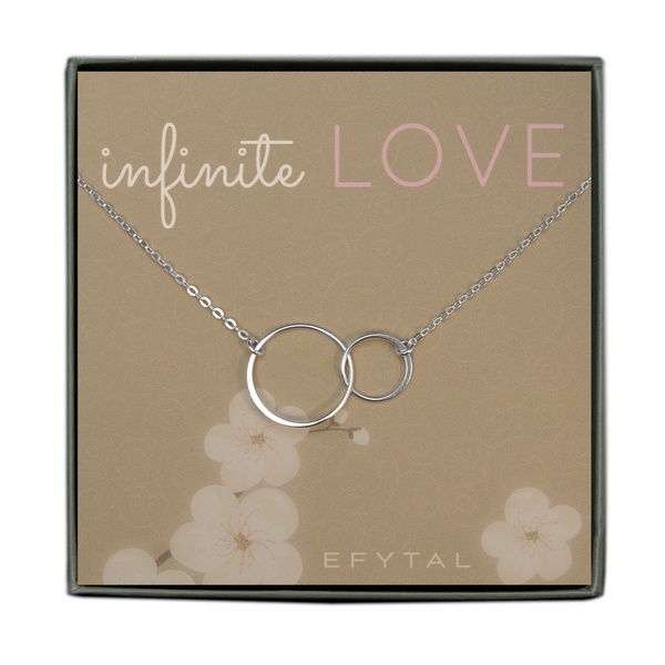 A grey jewelry box contains a beige message card with white swirl and flower motifs. A sterling silver necklace with two interlocking thin rings rests on the card. The text at the top of the card reads "infinite LOVE" in white and pink. The text in the bottom corner of the card reads "EFYTAL"