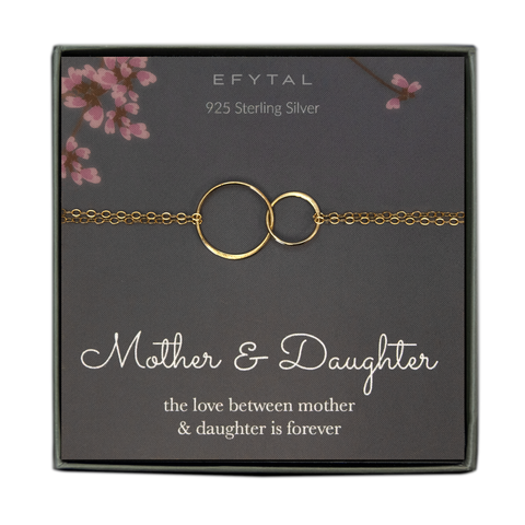 A grey jewelry box holds a grey message card with pink flower motif at the top. A 14k gold fill bracelet with two joined rings rests on the card. The text above the necklace reads "EFYTAL 925 Sterling Silver" in cream text. Underneath the necklace, the text reads "Mother & Daughter the love between mother & daughter is forever"