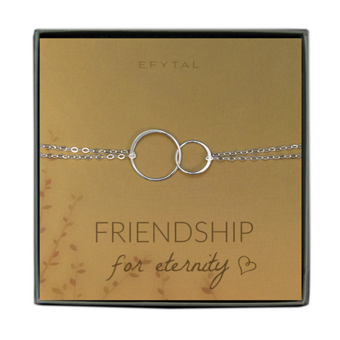 A green jewelry box holds a yellow jewelry card with brown leaf motif in the bottom left corner. A sterling silver bracelet with two interlocked silver rings rests on the card. The text above the jewelry reads "EFYTAL" in brown font, and below the necklace the card says "FRIENDSHIP for eternity <3"