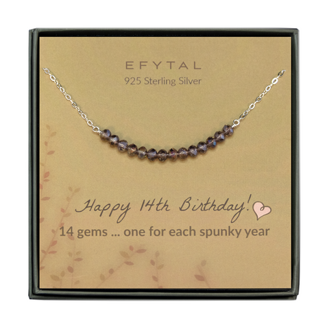  grey jewelry box containing silver necklace with fourteen iridescent purple glass beads, placed on a faded yellow card with a branch motif in the lower left corner. the text on the card reads "EFYTAL 925 sterling silver" in brown at the top and "Happy 14th Birthday! 14 gems...one for each spunky year" at the bottom.