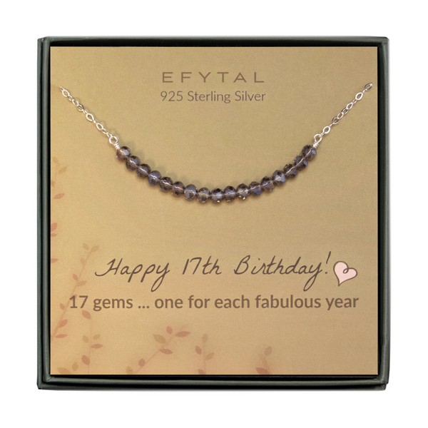  grey jewelry box containing silver necklace with seventeen iridescent purple glass beads, placed on a faded yellow card with a branch motif in the lower left corner. the text on the card reads "EFYTAL 925 sterling silver" in brown at the top and "Happy 17th Birthday! 17 gems...one for each fabulous year" at the bottom.