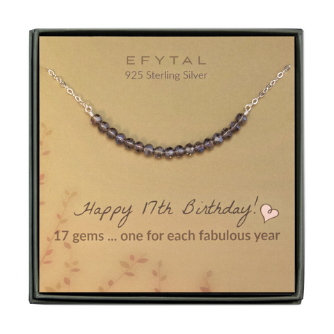  grey jewelry box containing silver necklace with seventeen iridescent purple glass beads, placed on a faded yellow card with a branch motif in the lower left corner. the text on the card reads "EFYTAL 925 sterling silver" in brown at the top and "Happy 17th Birthday! 17 gems...one for each fabulous year" at the bottom.