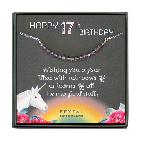 grey jewelry box containing silver necklace with seventeen iridescent purple glass beads, placed on a grey card. The bottom left corner of the card has a unicorn and roses, there is a rainbow in the bottom center, and a rose on the bottom right corner. The card reads "Happy 17th birthday" in pink and white font at the top, and "Wishing you a year filled with rainbows and unicorns and all the magical stuff <3" underneath in white. "EFYTAL 925 sterling silver" is in small dark text at the bottom of the card. 