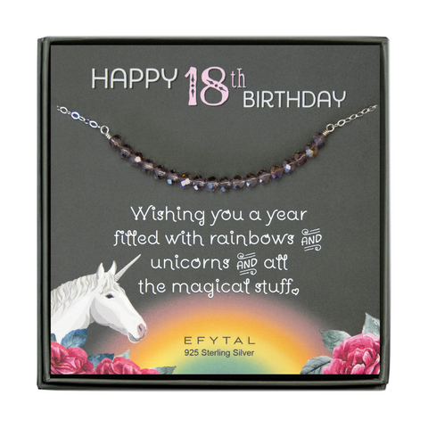 grey jewelry box containing silver necklace with eighteen iridescent purple glass beads, placed on a grey card. The bottom left corner of the card has a unicorn and roses, there is a rainbow in the bottom center, and a rose on the bottom right corner. The card reads "Happy 18th birthday" in pink and white font at the top, and "Wishing you a year filled with rainbows and unicorns and all the magical stuff <3" underneath in white. "EFYTAL 925 sterling silver" is in small dark text at the bottom of the card. 