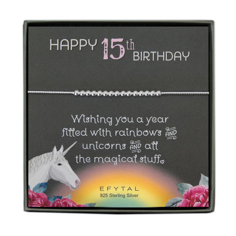 grey jewelry box containing silver bracelet with fifteen round silver beads, placed on a grey card. The bottom left corner of the card has a unicorn and roses, there is a rainbow in the bottom center, and a rose on the bottom right corner. The card reads "Happy 15th birthday" in pink and white font at the top, and "Wishing you a year filled with rainbows and unicorns and all the magical stuff <3" underneath in white. "EFYTAL 925 sterling silver" is in small dark text at the bottom of the card. 