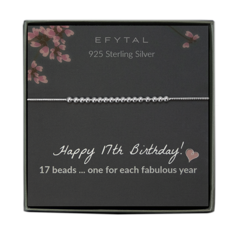  grey jewelry box containing a silver bracelet with seventeen round silver beads, placed on a grey card with pink flowers at the top. the text on the card reads "EFYTAL 925 sterling silver" at the top and "Happy 17th Birthday! <3 17 beads... one for each fabulous year" at the bottom.