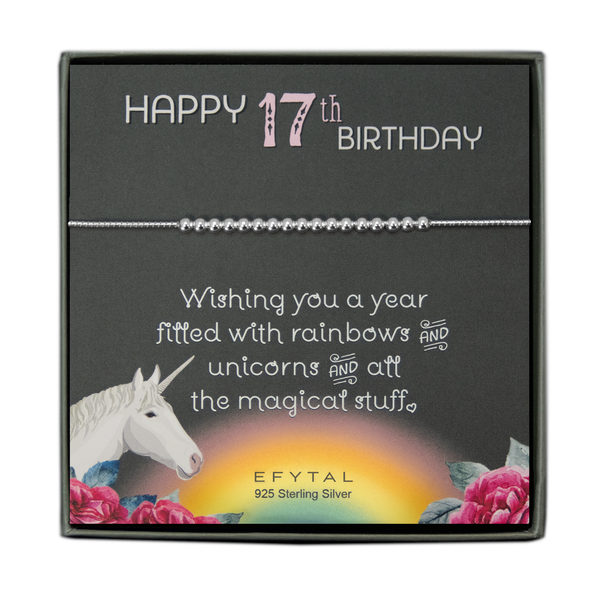 grey jewelry box containing silver bracelet with seventeen round silver beads, placed on a grey card. The bottom left corner of the card has a unicorn and roses, there is a rainbow in the bottom center, and a rose on the bottom right corner. The card reads "Happy 17th birthday" in pink and white font at the top, and "Wishing you a year filled with rainbows and unicorns and all the magical stuff <3" underneath in white. "EFYTAL 925 sterling silver" is in small dark text at the bottom of the card. 