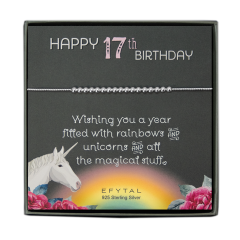 grey jewelry box containing silver bracelet with seventeen round silver beads, placed on a grey card. The bottom left corner of the card has a unicorn and roses, there is a rainbow in the bottom center, and a rose on the bottom right corner. The card reads "Happy 17th birthday" in pink and white font at the top, and "Wishing you a year filled with rainbows and unicorns and all the magical stuff <3" underneath in white. "EFYTAL 925 sterling silver" is in small dark text at the bottom of the card. 