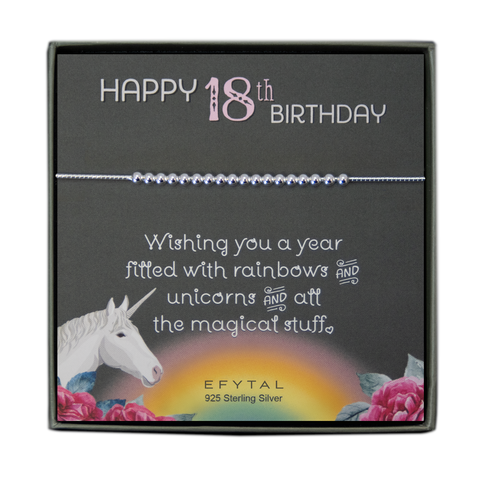 grey jewelry box containing silver bracelet with eighteen round silver beads, placed on a grey card. The bottom left corner of the card has a unicorn and roses, there is a rainbow in the bottom center, and a rose on the bottom right corner. The card reads "Happy 18th birthday" in pink and white font at the top, and "Wishing you a year filled with rainbows and unicorns and all the magical stuff <3" underneath in white. "EFYTAL 925 sterling silver" is in small dark text at the bottom of the card. 