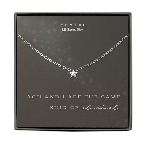 A grey jewelry box containing a grey message card with a star motif extending diagonally across the card. A silver necklace with a small silver star pendant rests on the card. The white text at the top of the card reads “EFYTAL 925 Sterling Silver” and the text underneath the necklace reads “YOU AND I ARE THE SAME KIND OF stardust.”