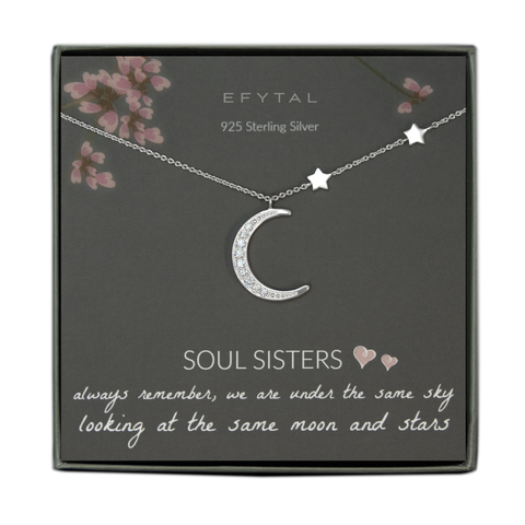 A grey jewelry box contains a grey message card with pink floral motif at the top. A silver necklace with two star stationed beads along the right side and a large crescent moon pendant with embedded CZ stones rests across the card. At the top in white font, the card reads "EFYTAL 925 Sterling Silver." At the bottom, it reads "SOUL SISTERS <3 <3 always remember, we are under the same sky looking at the same moon and stars"